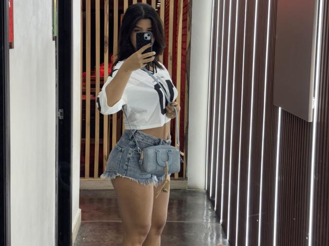 ScarlletZhen in a white shirt with black stripes, denim shorts, and a blue mini purse, holding a phone, showing her curvy ass and small tits, in a mirror selfie.