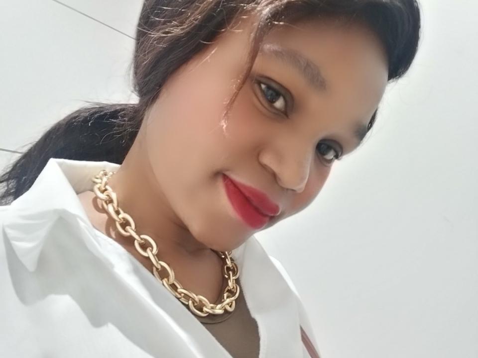 CherrryOnTop, con i capelli scuri raccolti in una coda di cavallo, che indossa rossetto rosso e una collana a catena dorata, sorride alla fotocamera, indossando una camicia bianca, in un selfie..