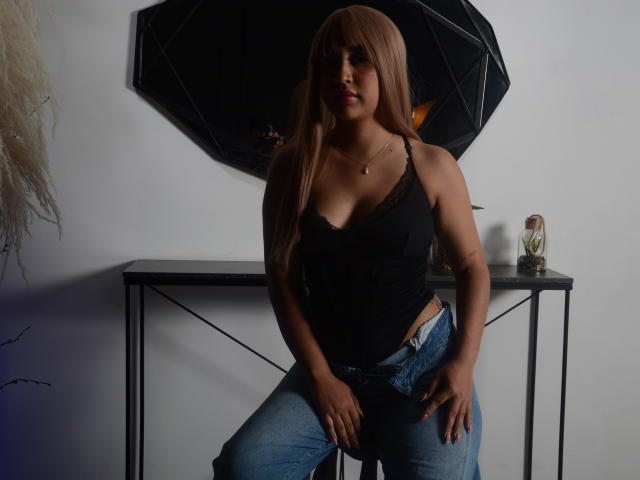 IvyBrooks with long brown hair, black tank top, showing her tits, in blue jeans, standing in front of a black mirror, hands on her jeans, confident, sexy, dark room.