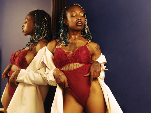 DaniaMarcell with dark skin and blue braids, wearing red lace bra and high-cut panties, white shirt off, tattoos on chest and hand, reflection in mirror, confident pose.