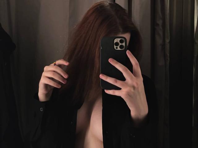 Yevette Cabrales maakt een spiegelzelfportret met een telefoon, zwarte blouse open, waardoor haar borsten zichtbaar zijn, bruin haar bedekt haar gezicht, rechterhand in haar haar, linkerhand houdt de telefoon vast..