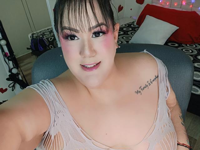 GiiannaMorrys con maquillaje rosa en los ojos, sonriendo, mostrando sus pechos en una blusa rosa rasgada, aro en la nariz, tatuaje en el hombro derecho y cabello corto negro, en un selfie..