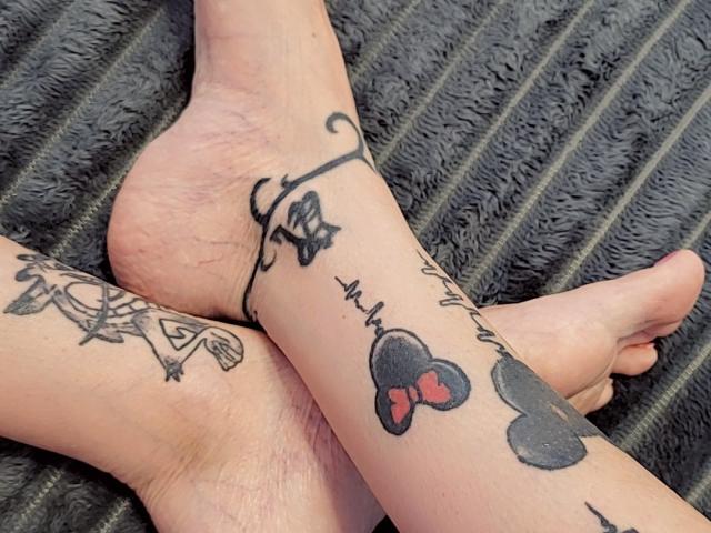 ElixirShanna's tattooed feet, showing black ink tattoos: a key on one ankle, a butterfly with red bow on the other, and a floral design on the left ankle.