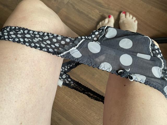 Bourgeoisex's black polka-dot panties, semi-sheer with white circles, are pulled down to her thighs, exposing her pale skin and red-painted toenails on a wooden floor.