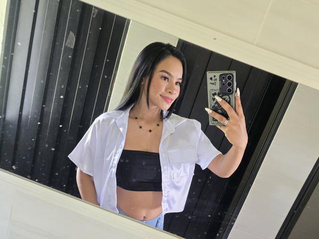 Yurimy with long black hair, wearing an open white shirt and black tube top, showing her small tits and smiling at a mirror selfie with a phone.