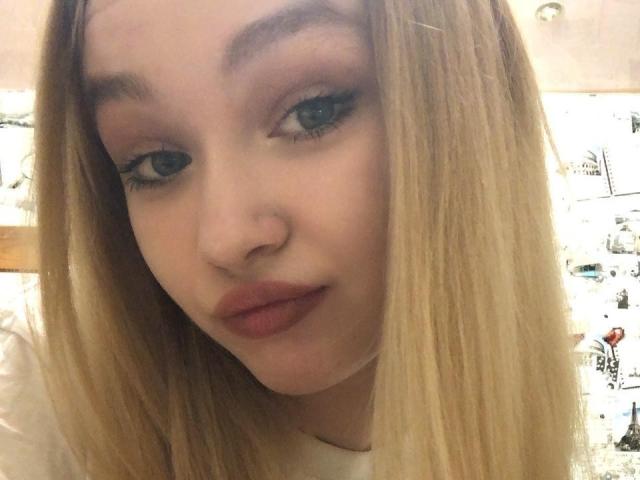AnnamaeSvehla has blonde hair, blue eyes, and pink lipstick with a nose piercing. Her full lips are slightly parted. She's wearing a white shirt. Her eyelashes are long.