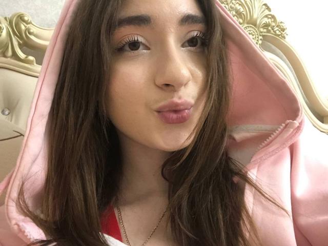 LiliaBilka, con i capelli castani, una felpa rosa, labbra piene e occhi marroni, indossa una maglietta rossa e una collana dorata, in un selfie. Il suo seno non è visibile..