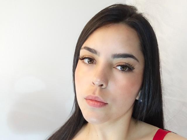 LaurynBm heeft lang zwart haar, bruine ogen en volle, roze lippen. Ze draagt een rode top, heeft een lichte glans op haar gezicht en draagt oordopjes..