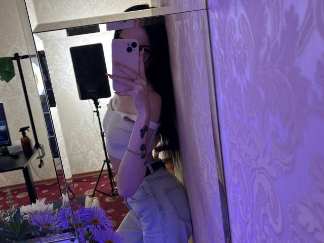 SamantaBredShow with long black hair, white ribbed top, and high-waisted jeans, taking a mirror selfie, showing her ass and a tattoo on her left arm.