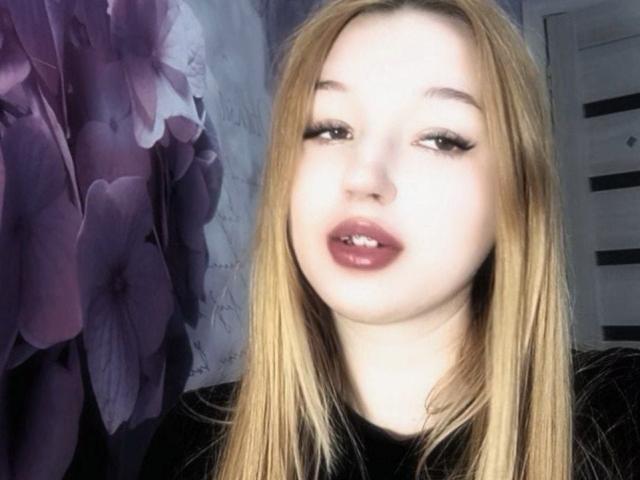 PenelopeOunsy with pale skin, blonde hair, and pink lipstick, looking slightly open-mouthed with dark, half-closed eyes, wearing a black top.