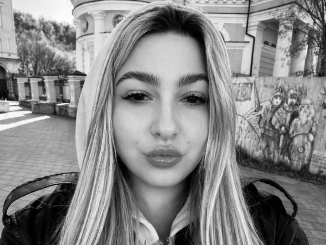 Schwarz-weißes Foto von DawnErika mit langen, glatten, blonden Haaren, vollen Lippen und einem leichten Schmollmund, die eine Kapuzenjacke trägt; ihre dicken Augenbrauen und das dezente Make-up sind auffällig..