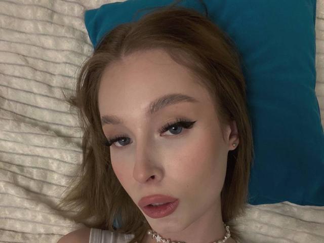 Ceola Goodroe tiene el cabello castaño claro, ojos azules y labios rosados y carnosos. Está acostada en una cama con una almohada azul, lleva un collar y parece un poco aburrida..