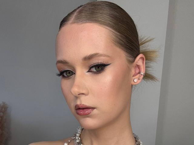 Lilliana Whang hat glattes, zurückgebundenes blondes Haar, grüne Augen, dicken schwarzen Eyeliner, rosafarbene, glänzende Lippen, hellen Teint und einen kleinen Nasenring in ihrem rechten Ohr. Sie trägt eine glitzernde Halskette..