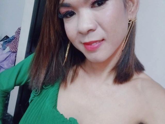 SuperiorMistress-hot tiene senos de tamaño medio, lleva una blusa verde, aretes dorados y lápiz labial rojo, sonríe con cabello castaño de largo medio y labios ligeramente entreabiertos..