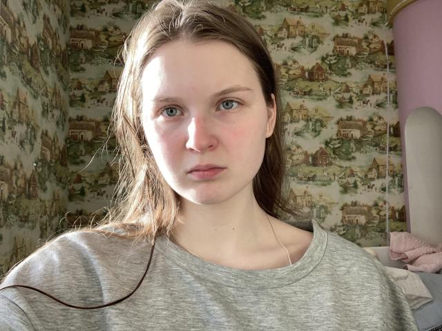 Jutta Hillwig, mit heller Haut, blauen Augen und braunen Haaren, trägt ein graues Hemd, hat einen neutralen Gesichtsausdruck und eine feine Halskette..