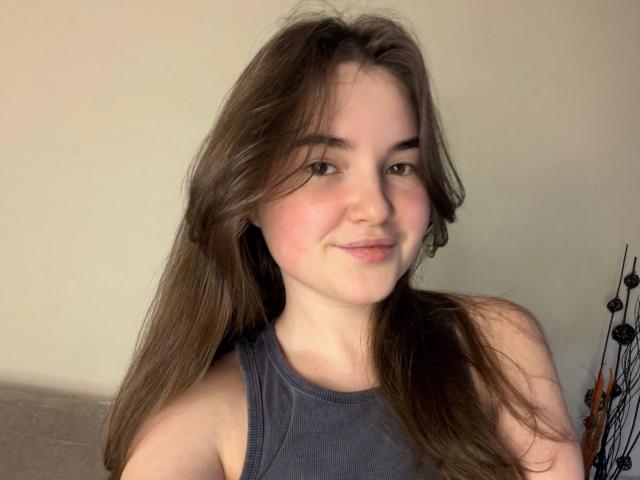 LizabethAmore, con lunghi capelli castani, pelle chiara e un leggero sorriso, indossa una canotta grigia che mette in mostra il seno, in un selfie casuale..