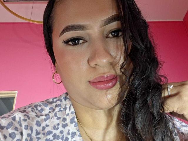 Eine lateinamerikanische Frau mit nassen, schwarzen Haaren, Reifenohrringen und pinkem Lippenstift, hat eine kleine Piercing am Unterlippen, trägt ein Leopardenmuster-Shirt und schaut in die Kamera..