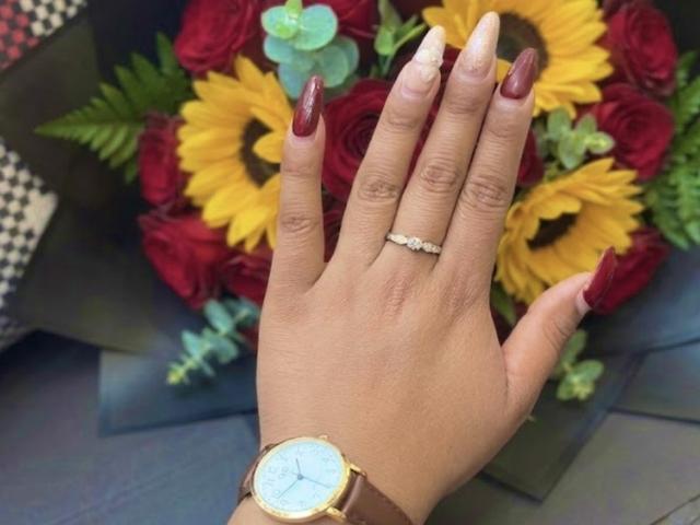 La mano di SophieSonyas, con unghie di rosso scuro, un orologio d'oro e un anello di diamanti, che tiene un bouquet di girasoli, rose rosse ed eucalipto..