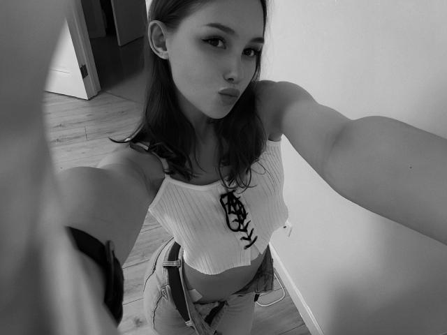 Black-and-white selfie of AnyaRuivo with medium tits, wearing a ribbed crop top with lace-up front, and plaid pants, standing in a room with wooden floors.