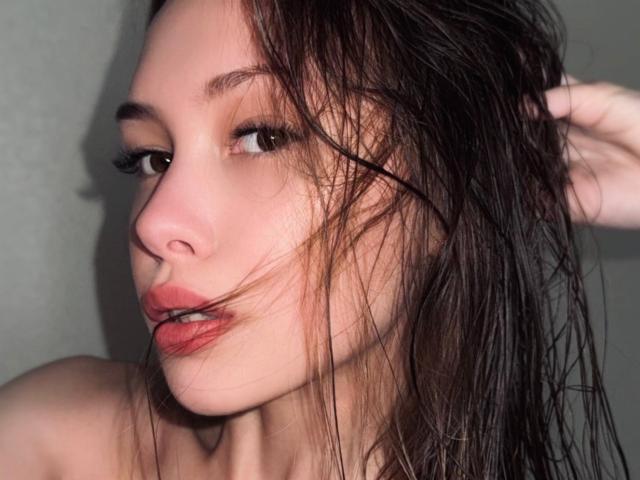AnyaRuivo met nat bruin haar, lichtjes open lippen die een glimp van haar tanden laten zien, en bruine ogen die schuin naar de zijkant kijken. Haar neus is klein en haar huid is bleek..