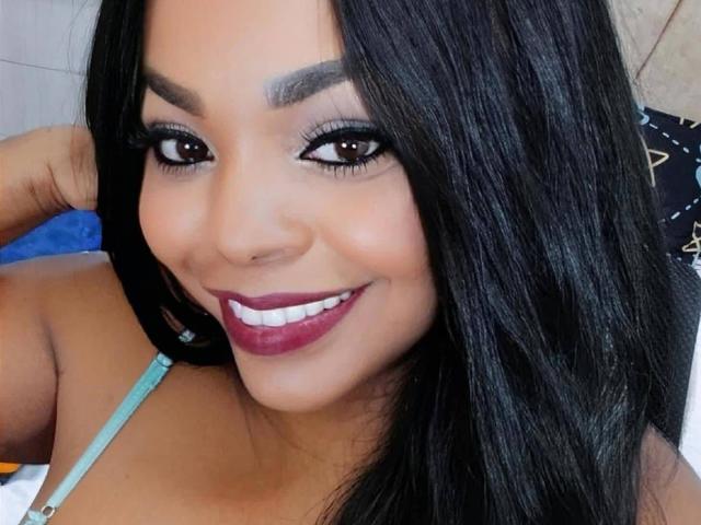 Tatiana Marin, avec ses cheveux noirs brillants, ses yeux marron foncé, ses sourcils épais, son rouge à lèvres violet et son piercing mignon sur le nez, sourit à l'appareil photo, montrant sa poitrine dans un haut bleu à bretelles..