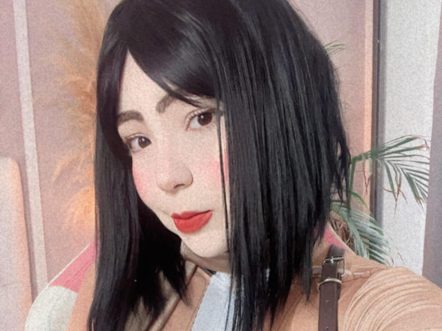 LizzyPortman con un corte de pelo recto y negro, lápiz labial rojo, piel pálida, ojos marrones, vistiendo una blusa marrón, mirando a la cámara, con un ligero rubor en las mejillas, nariz pequeña, luz suave, labios voluminosos..