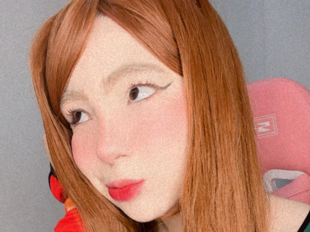 Lizy Portman ha i capelli rossi, la pelle chiara e il rossetto rosso. Guarda di lato con l'eyeliner ad ali di farfalla, e il suo naso leggermente all'insù ha una sfumatura rosa. È seduta su una sedia rosa..