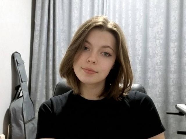 JennellMatacale, with light brown bob, wearing black shirt, has small ass, slight smile, and light skin, sitting in chair, looking at camera.
