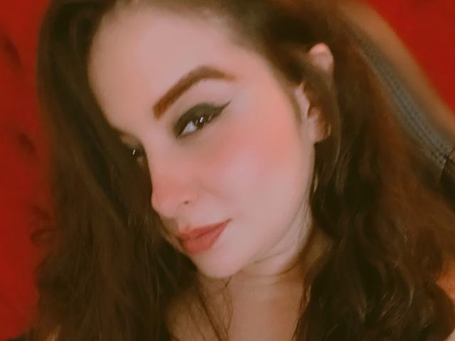 ValentinaCoba tiene el cabello castaño ondulado, cejas pobladas y delineador de ojos oscuro. Se puede ver su colorete rosa y sus labios rojos. Está mirando hacia abajo con una ligera sonrisa..