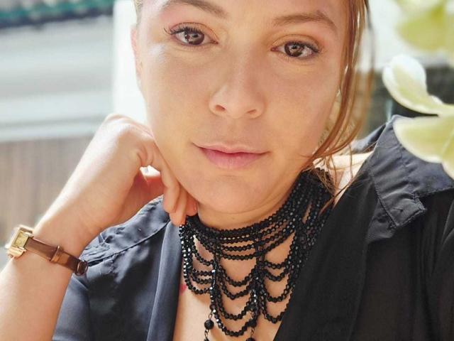 MoonXVelvet with brown eyes, light skin, and subtle pink eyeshadow, wearing a black necklace and black shirt, has a brown wristwatch on her right wrist, looking at camera.