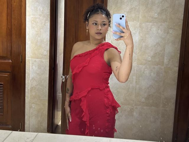 SofiaPassionne, Asian woman with curly hair, wearing a red, ruffled off-shoulder dress, holding a blue phone in a bathroom mirror selfie, showing her tits and ass.