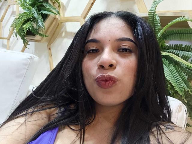 SammyRossek with long black hair, pouty pink lips, brown eyes, and a tan complexion, wearing a purple top, looking directly at the camera.