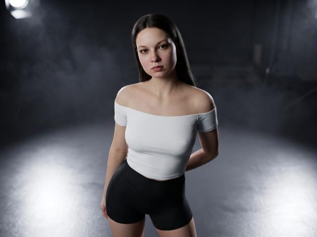 KrisEmpey with long black hair, off-shoulder white top, and black shorts, standing, hands behind back, neutral expression, dark background, subtle light flares.