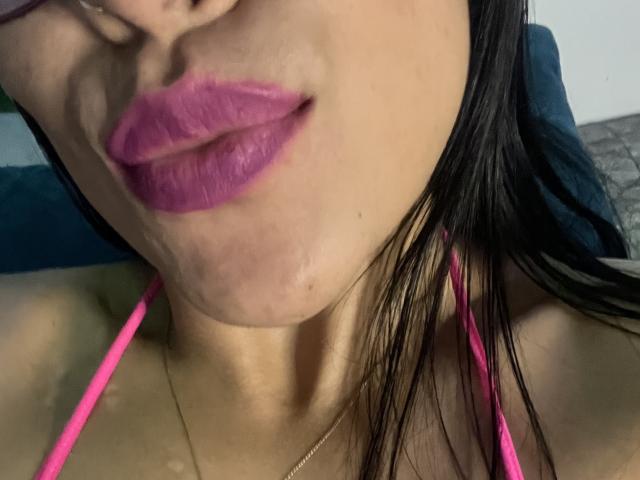 StellaBeckker's pink lipstick, slightly parted glossy lips, small chin, black straight hair, pink halter straps, tan skin, and a subtle neck tattoo are visible in the image.