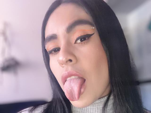 StellaBeckker ha lunghi capelli neri, ombretto arancione e eyeliner nero ad ali di gabbiano. Ha la lingua rosa fuori e un piccolo piercing al naso nella narice sinistra..