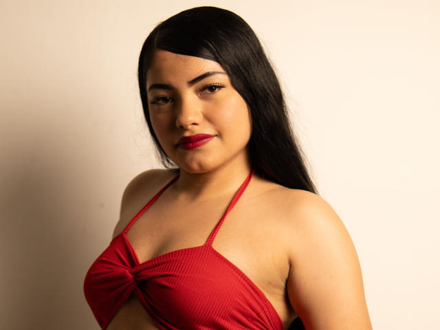 BrianaClarkX with long black hair, red halter top, showing her tits, red lipstick, slight smile, tan skin, soft light, centered in the frame.