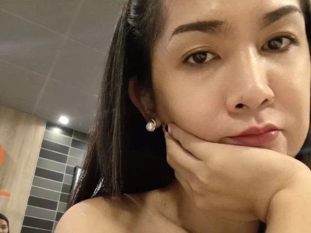 MissKinkyWild-hot has dark eyes, brown hair, and wears diamond earrings, resting her cheek on her hand with a subtle smile, showing her nose piercing.