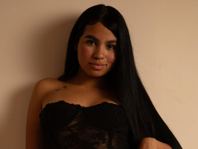 Dalila Tennesse tiene el pelo largo y negro, un piercing en la nariz, y lleva un top negro de encaje sin tirantes que deja ver sus pechos y un pequeño tatuaje en el hombro derecho..