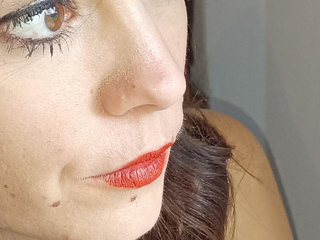 De neus van OrianaLaFrancaise staat in de schijnwerpers, met rode lippenstift, bruine ogen en donkere wimpers. Haar huid heeft een paar kleine moedervlekken en haar bruine haar is gedeeltelijk zichtbaar..