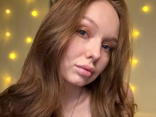 NieshaRonsini has light brown hair, a nose ring, and pouty pink lips. She's looking slightly to the side with soft, fair skin and blue eyes. Boobs not visible.