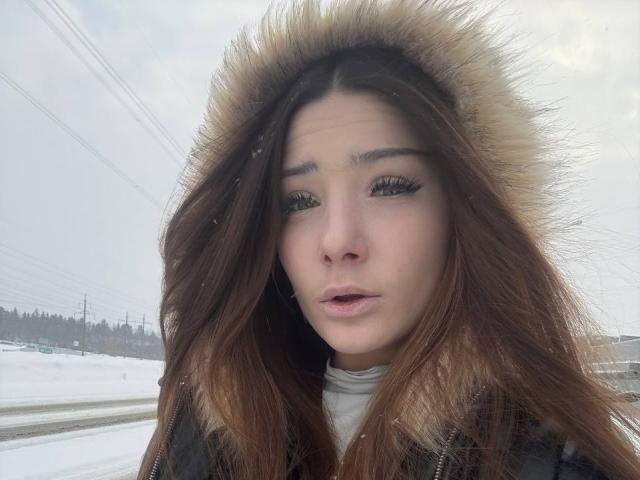 Angie Plassmeyer, con lunghi capelli castani, indossa un cappotto nero con bordo di pelliccia, appare leggermente confusa, con le extension alle ciglia ben visibili, e si trova in un paesaggio innevato..