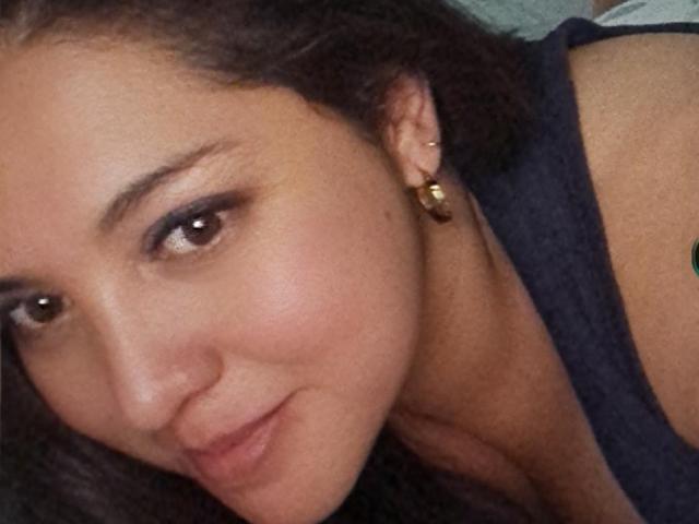 Paula tiene la piel de un marrón medio, cabello rizado oscuro, ojos marrones y una ligera sonrisa. Lleva una blusa negra con aretes dorados. Su rostro está cerca de la cámara..