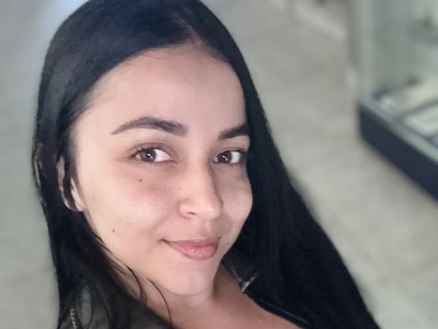 HikariChloe has long black hair, brown eyes, and a slight smile with pink lips. Her face shows a small mole on her left cheek. She's wearing a green top.