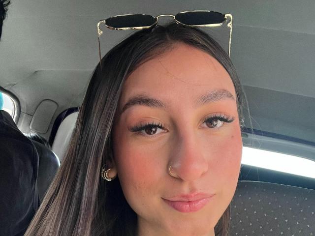 MaddyCarina with long brown hair, glasses on head, nose ring, and pink lips, smiling slightly, showing off her big brown eyes and full eyelashes.