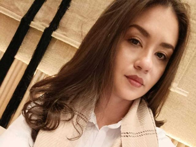 TheresaLarson has brown hair, a cute face, and a subtle smile. She's wearing a white shirt with a beige plaid scarf. Her brown eyes look at the camera.