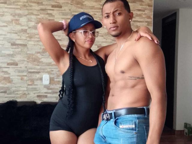 LilithAndAsmodeo with long black braids, glasses, and blue cap, wearing a black one-piece, stands next to shirtless LilithAndAsmodeo with blue jeans and a visible belt.