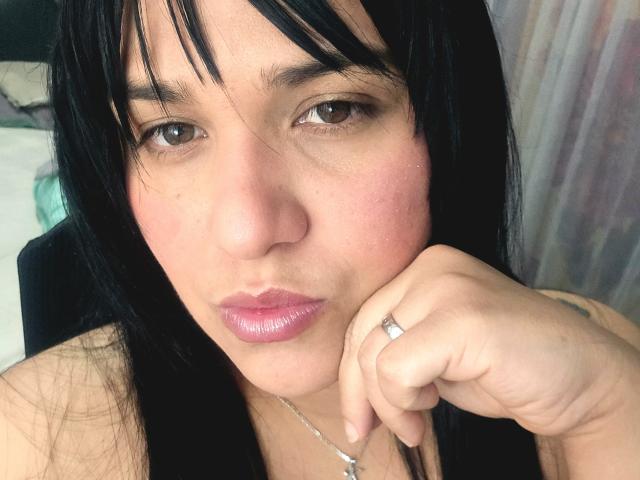 VivianaThompson has black hair, brown eyes, pinkish lips, and a ring on her right hand. Her hand is near her face with a slightly pouty expression.