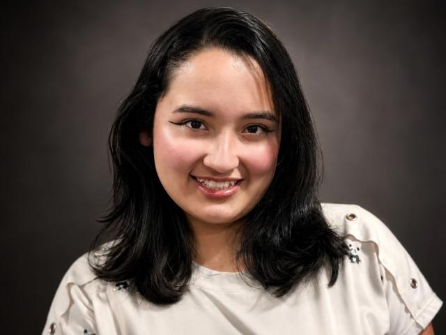 CristaLuxury heeft zwart, halflang haar, ze glimlacht met licht open lippen en draagt een witte blouse met kleine bloemmotieven. Ze heeft lichtbruine huid en zwarte eyeliner..