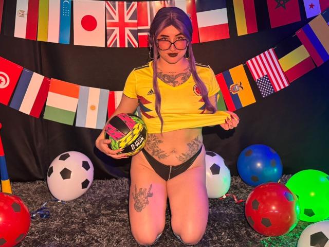 LilithDark69 de rodillas, usando gafas, camiseta amarilla de fútbol, ropa interior negra, sosteniendo un balón de fútbol, cabello morado, tatuajes, balones de fútbol, banderas coloridas, alfombra gris, luces de neón, sexy..