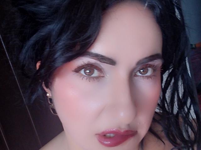 LuluFrancaise ha i capelli scuri e ondulati, gli occhi marroni e il rossetto rosso. Il suo viso è leggermente arrossato con il trucco rosa. Indossa orecchini dorati. Le sue labbra sono leggermente socchiuse..